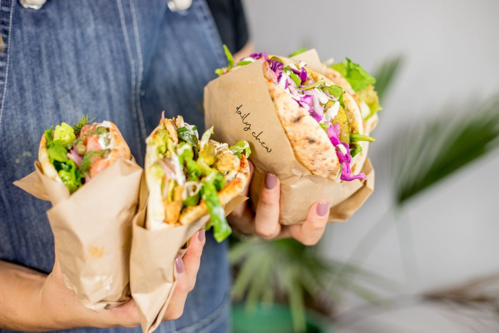 A close up of a woman's hands holding three deli wrapped sandwiches from Daly Chew in Atlanta.