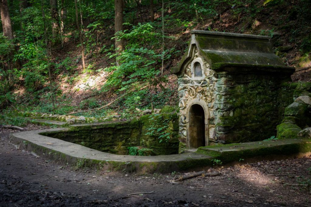 An ancient stone structure with a small arched doorway, nestled in a lush, moss-covered forest clearing in Atlanta, Georgia.