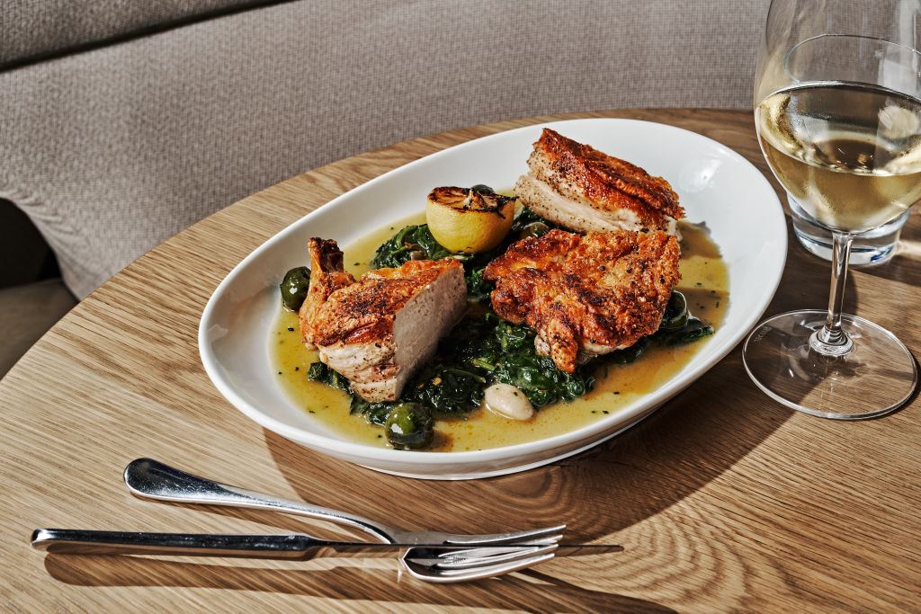 Where to Dine with a Large Group at Atlanta’s Michelin Guide Restaurants 8 A plate of crispy pork belly with greens and lemon slices, accompanied by a glass of white wine in Atlanta, Georgia.
