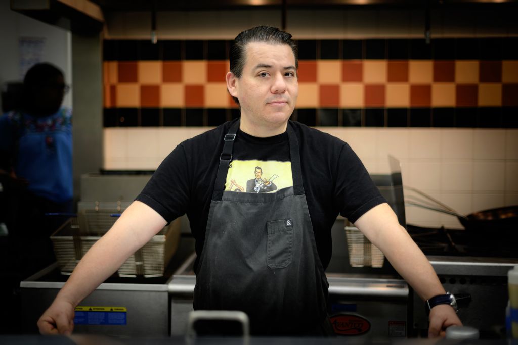 Chef standing in the kitchen wearing apron and black shirt. 