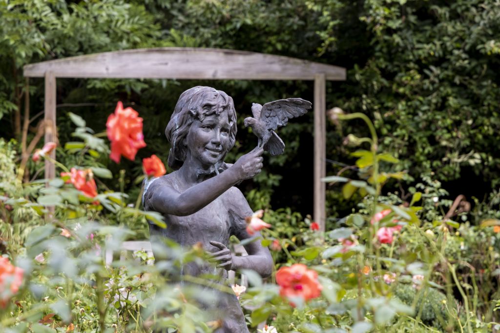 A bronze statue of a young girl with a bird perched on her hand, surrounded by colorful flowers in Atlanta, Georgia.