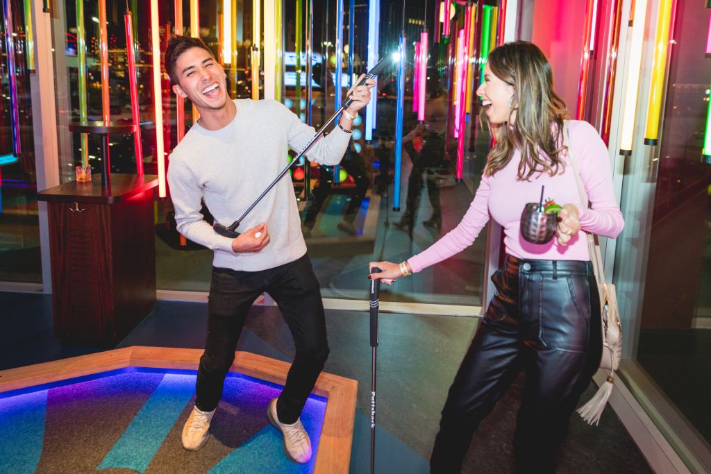 A man and woman play mini-golf in a brightly lit, colorful indoor course in Atlanta, Georgia.