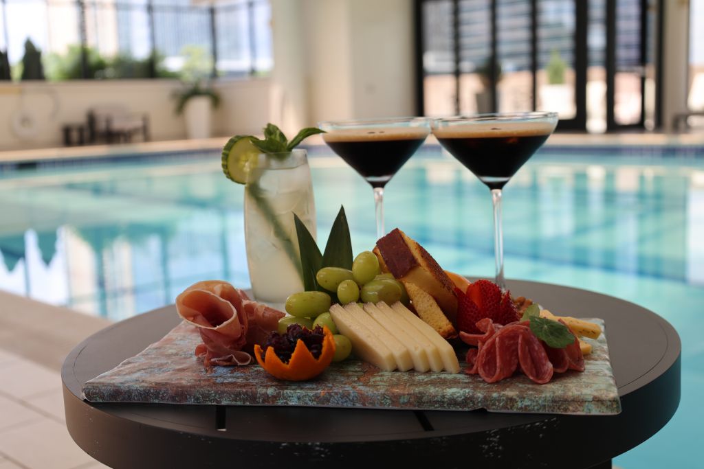 A poolside table with a martini glass, a glass of water with cucumber, and a charcuterie board in Atlanta, Georgia.