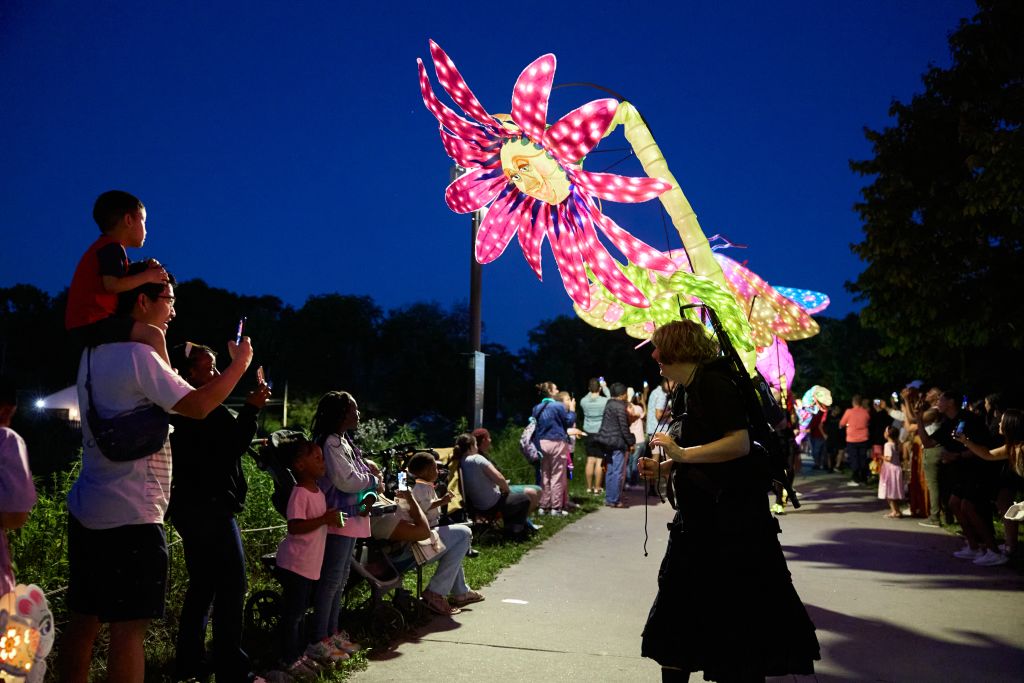 People gather at night to see illuminated flower sculptures along a path in Atlanta, Georgia.