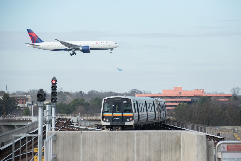 A Delta airplane flies above an elevated train track with a train passing underneath in Atlanta, Georgia.