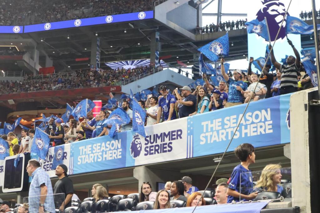 A crowded stadium with fans waving blue flags and banners celebrating the start of a summer sports series in Atlanta, Georgia.