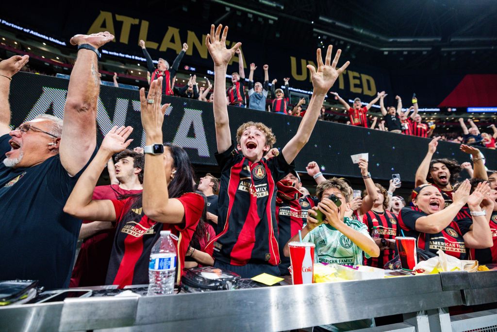A crowd of Atlanta United fans celebrates a goal with raised arms and enthusiastic cheers in Atlanta, Georgia.