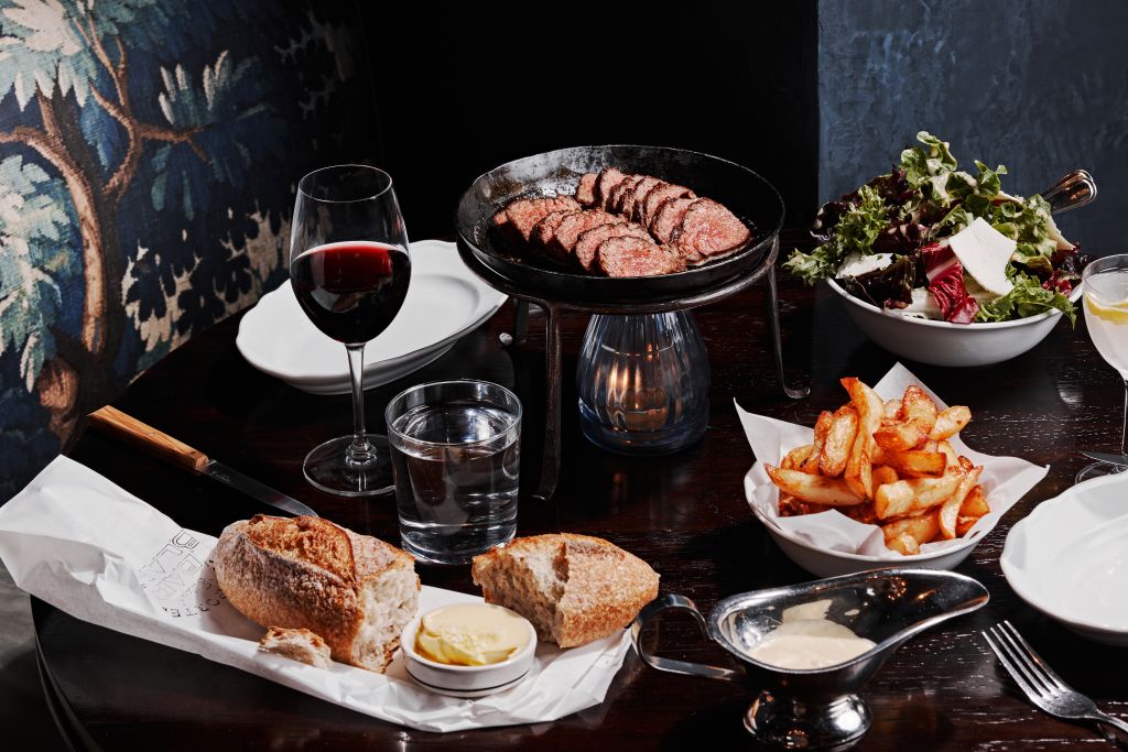 A table set with a variety of foods including steak, salad, bread, butter, fries, and wine in Atlanta, Georgia.