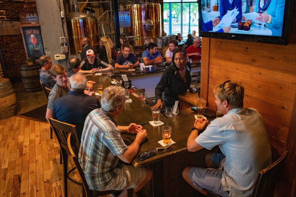 Patrons enjoy drinks at a crowded bar with a TV showing a news program in Atlanta, Georgia.