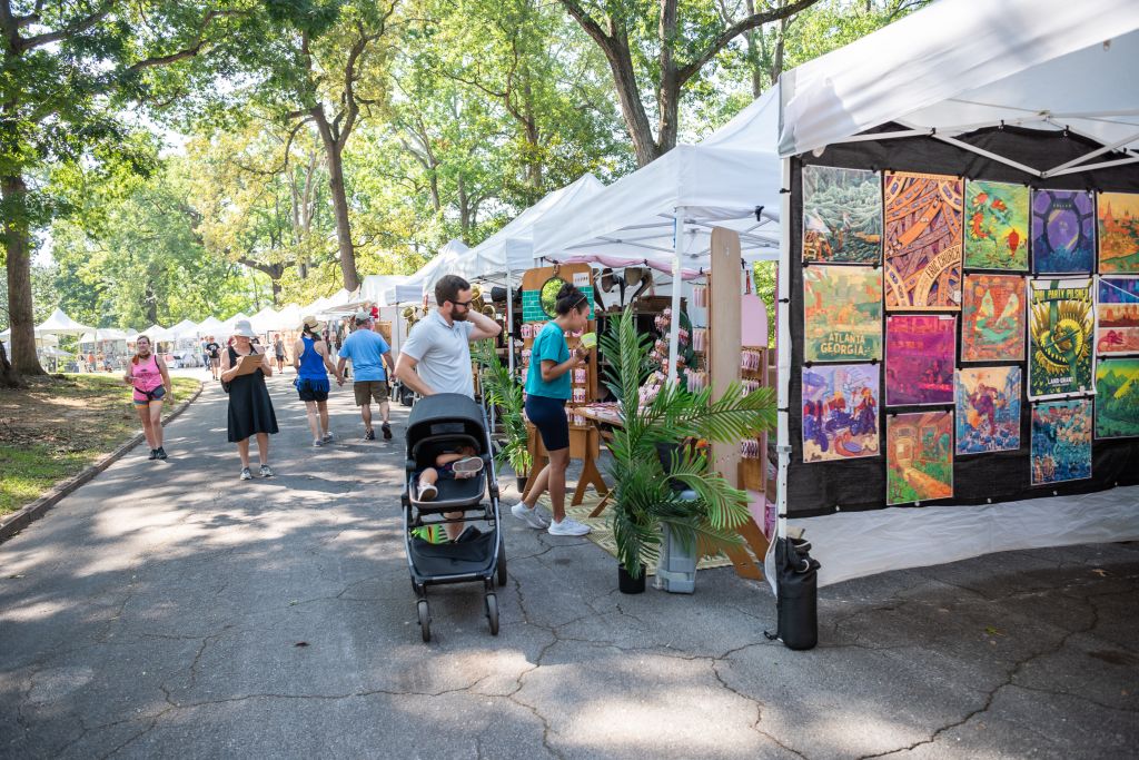 Outdoor art fair with colorful tents, paintings, and people strolling along a tree-lined path in Atlanta, Georgia.