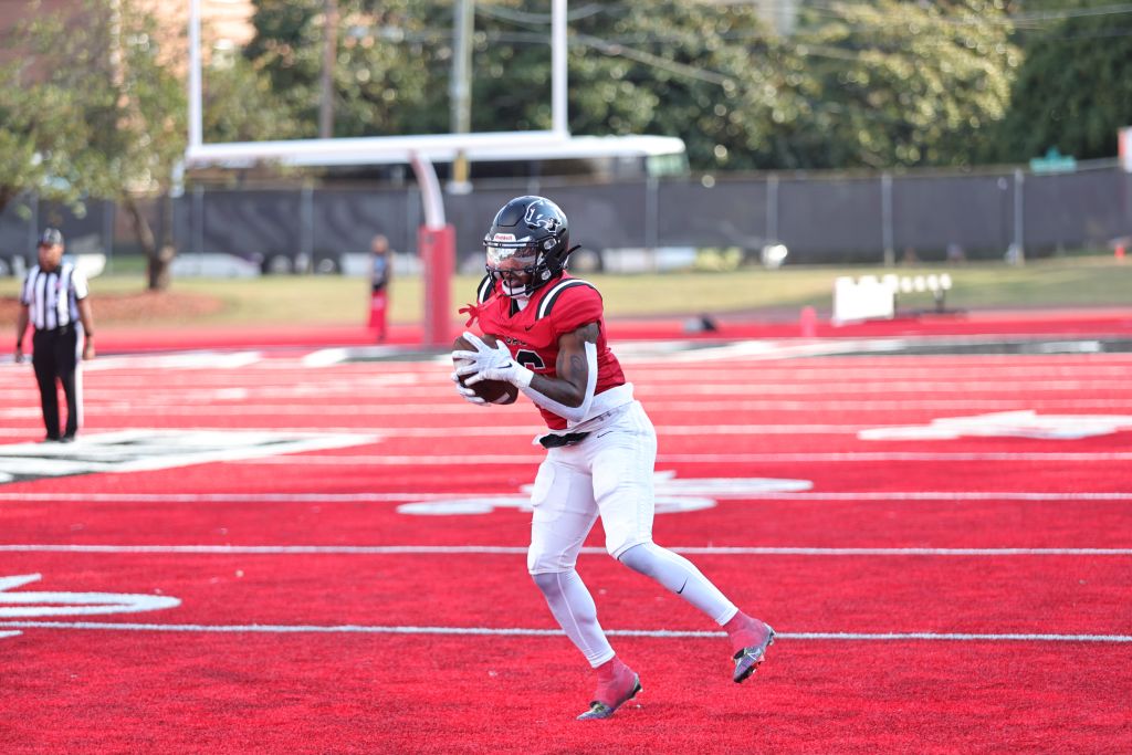 Football player in red uniform running with ball on red field in Atlanta, Georgia.