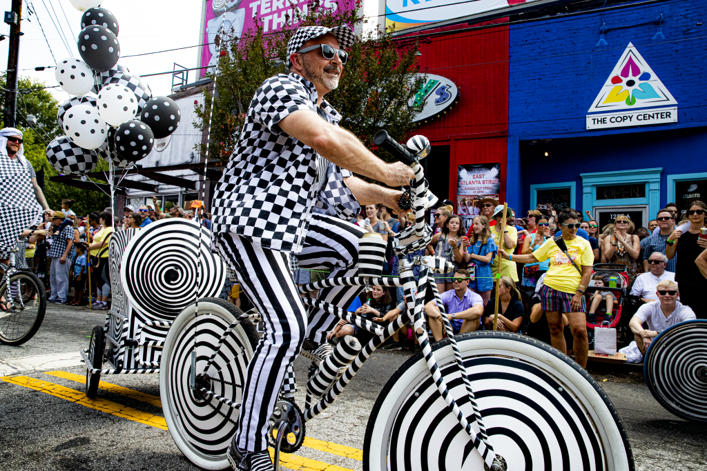 A man in a checkered outfit rides a black and white spiral-patterned bicycle in a parade in Atlanta, Georgia.
