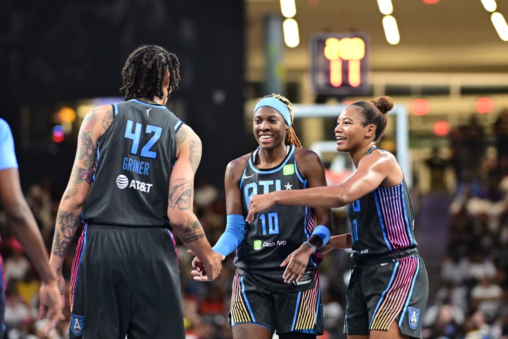 Three Atlanta Dream basketball players celebrate on the court with high fives in Atlanta, Georgia.