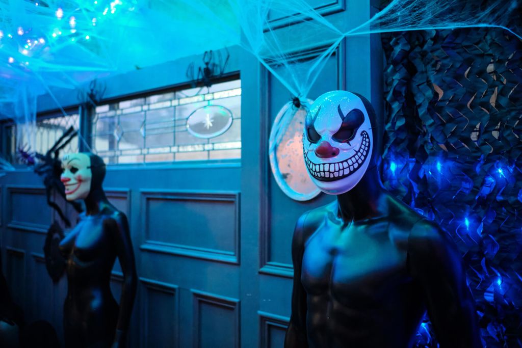 Two mannequins, one with a clown mask and another with a cat mask, stand in a dimly lit room decorated with blue lights and spiderwebs in Atlanta, Georgia.