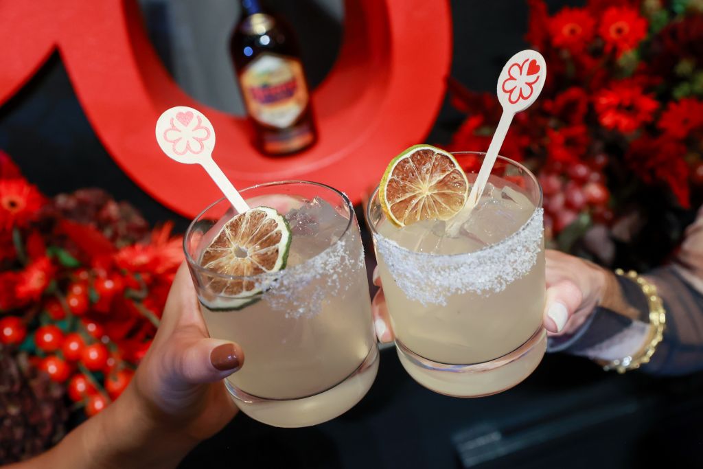 Two hands clinking glasses filled with a frothy, citrusy cocktail garnished with lime slices in Atlanta, Georgia.