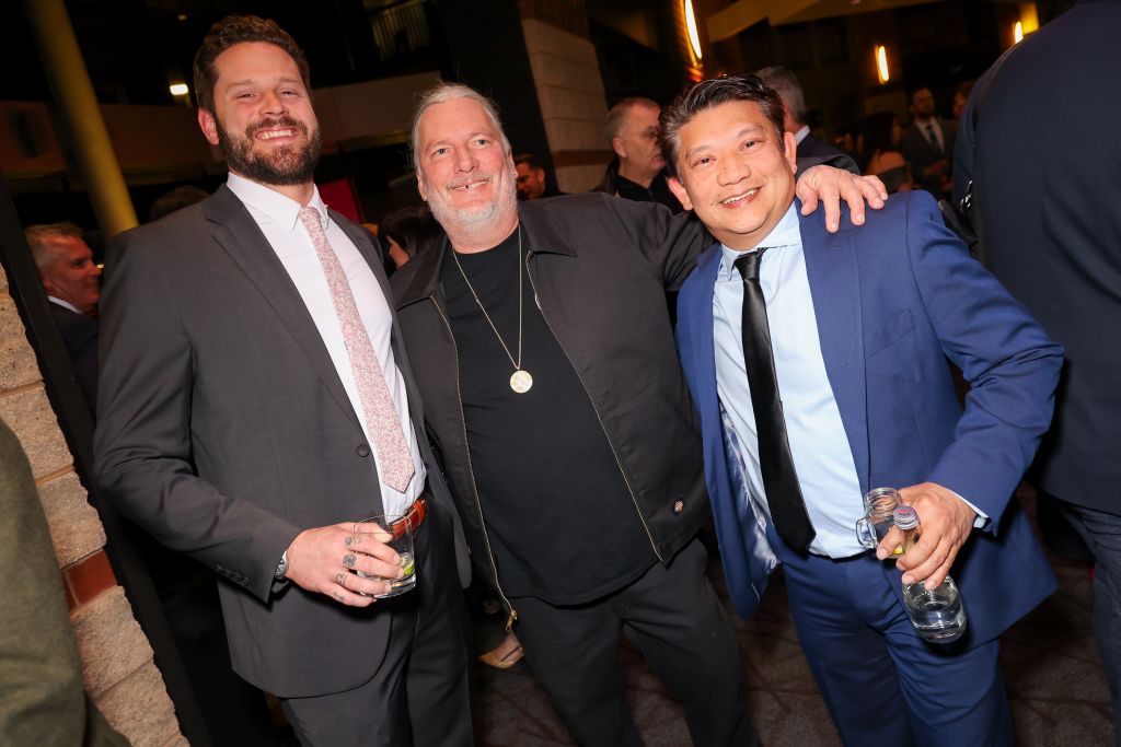 Three men in suits and ties, smiling and holding drinks at a social event in Atlanta, Georgia.