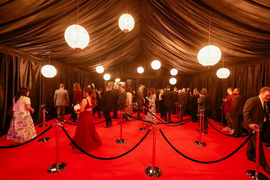 A formal event with guests dressed in evening wear walking on a red carpet under a black tent with hanging lights in Atlanta, Georgia.