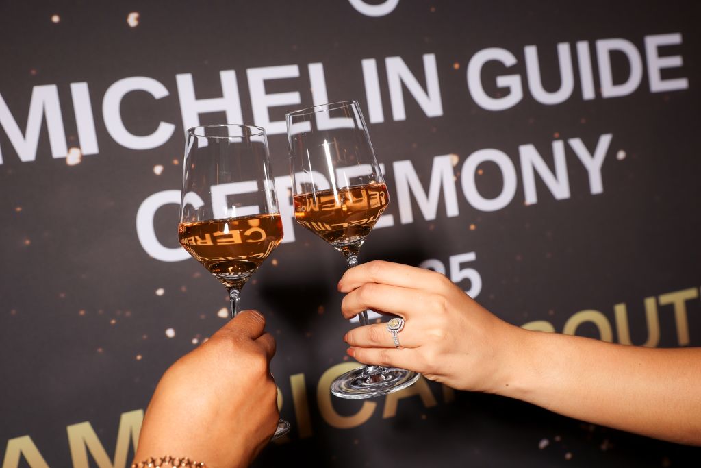 MICHELIN Guide Atlanta 2025 Awards 10 Two hands clink champagne glasses filled with rosé wine against a dark backdrop in Atlanta, Georgia.
