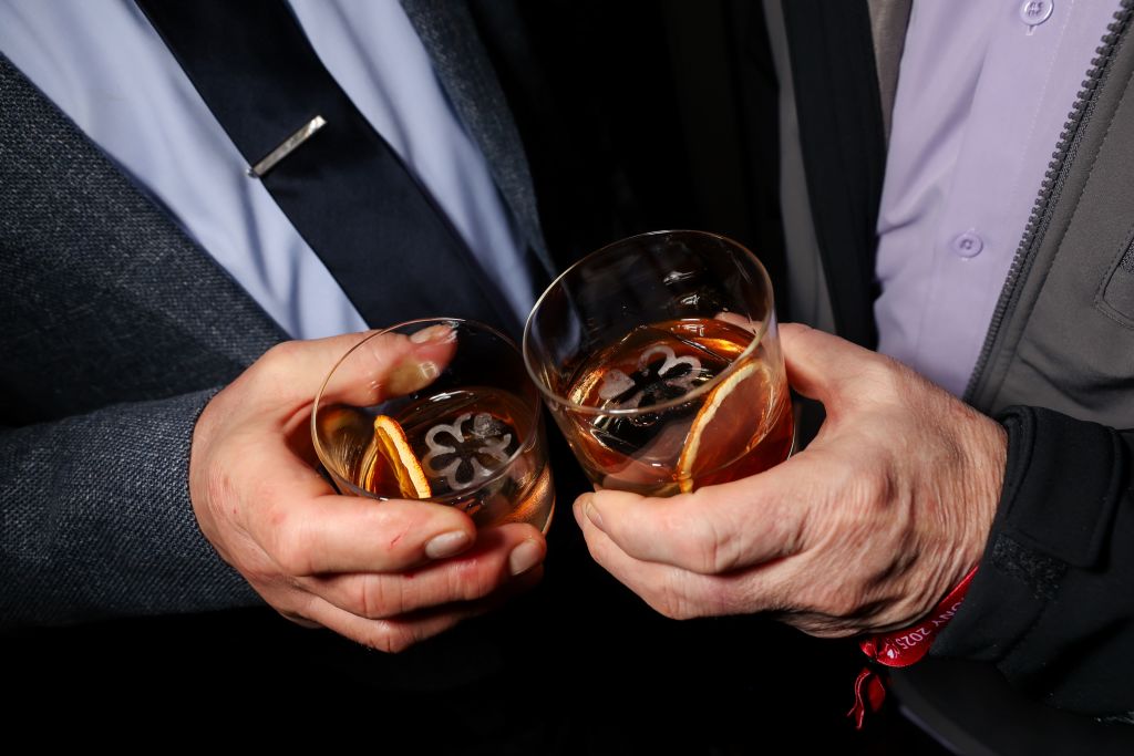 Two men in suits clink glasses filled with amber liquid and ice, garnished with orange slices in Atlanta, Georgia.