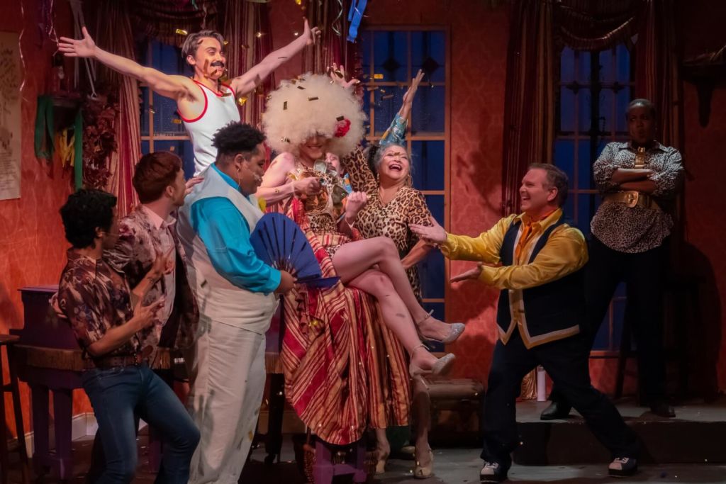 A lively stage scene with performers in colorful costumes dancing and celebrating in Atlanta, Georgia.