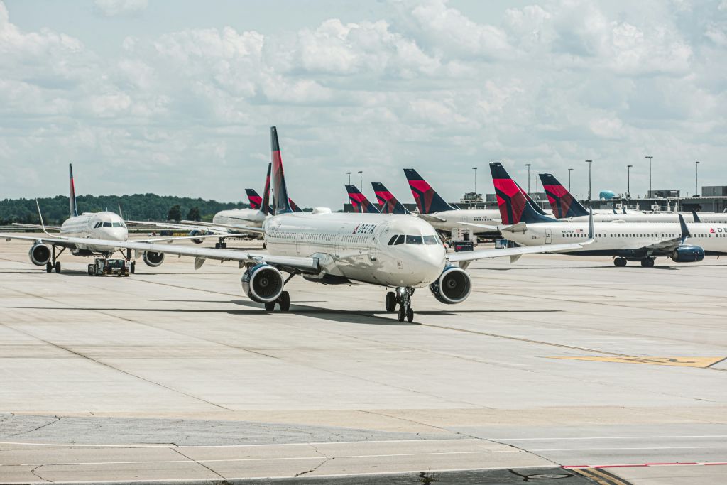 A row of Delta Air Lines airplanes are parked on the tarmac at an airport, with their distinctive red, white, and blue tails visible in Atlanta, Georgia.