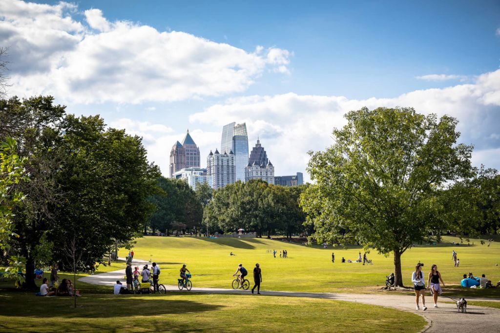 A vibrant city park filled with people enjoying a sunny day, with a stunning skyline of modern skyscrapers in the background in Atlanta, Georgia.