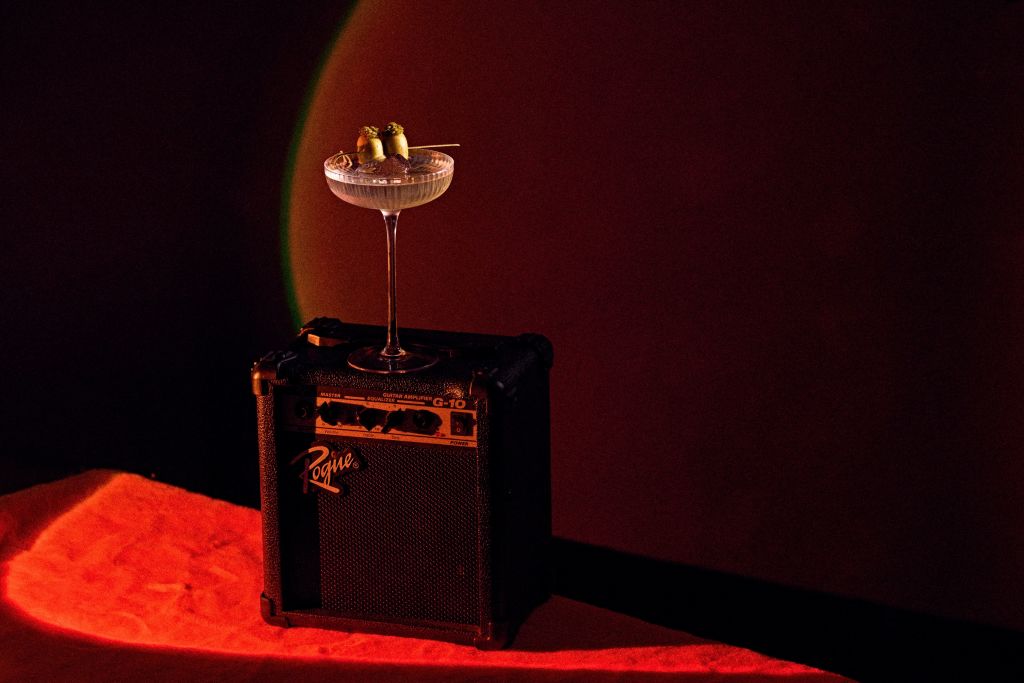 A martini glass with olives rests atop a small black amplifier, bathed in a warm red glow in Atlanta, Georgia.