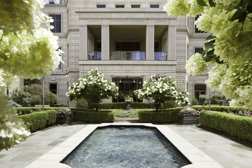 A serene courtyard features a rectangular pool surrounded by lush greenery and white flowers, with an elegant building in the background in Atlanta, Georgia.
