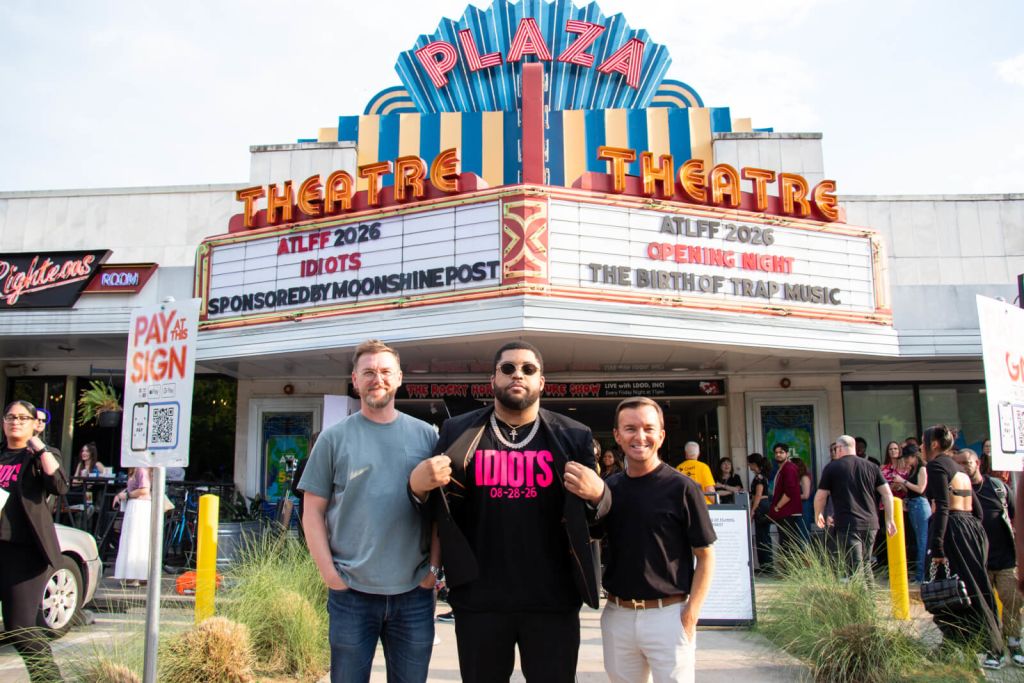 Three men stand in front of a vibrant, retro-style theater marquee advertising upcoming events in Atlanta, Georgia.
