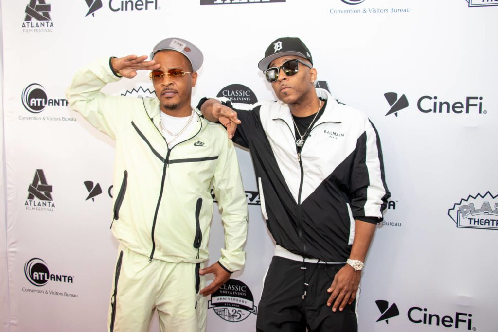 Two men dressed in matching tracksuits pose for a photo at an event, one saluting and the other pointing towards the camera in Atlanta, Georgia.
