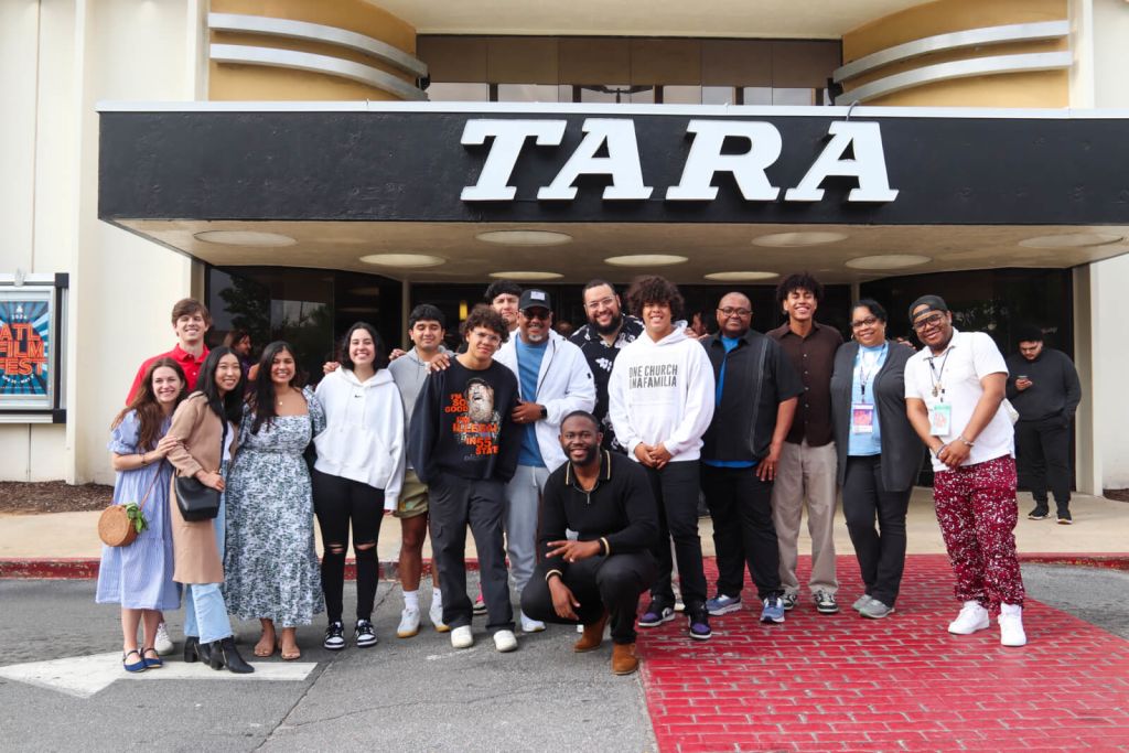 A diverse group of people pose for a photo in front of the TARA theater, smiling and dressed in casual attire in Atlanta, Georgia.