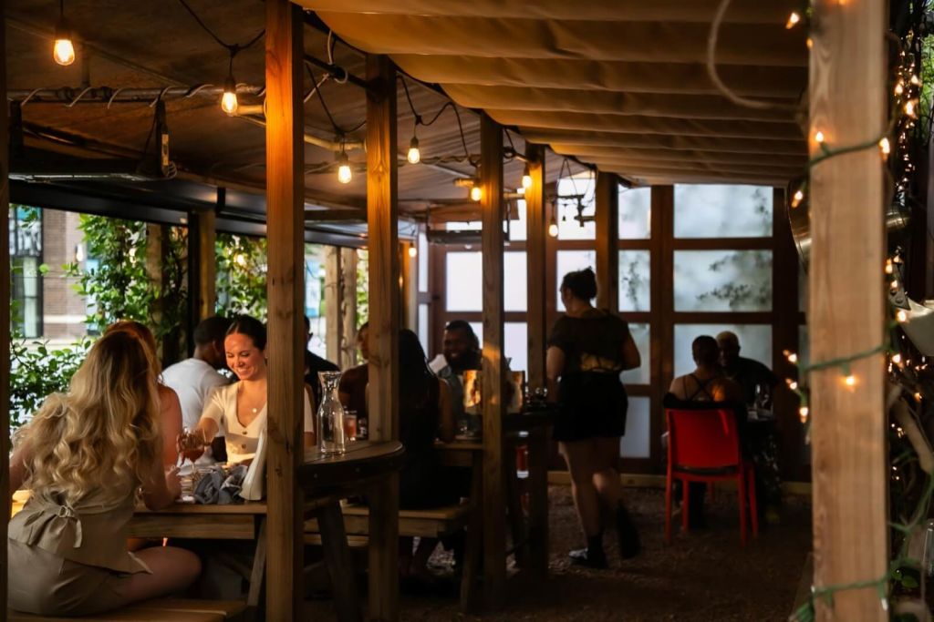 A cozy outdoor dining area with wooden beams and string lights, where people are enjoying meals at tables surrounded by greenery in Atlanta, Georgia.