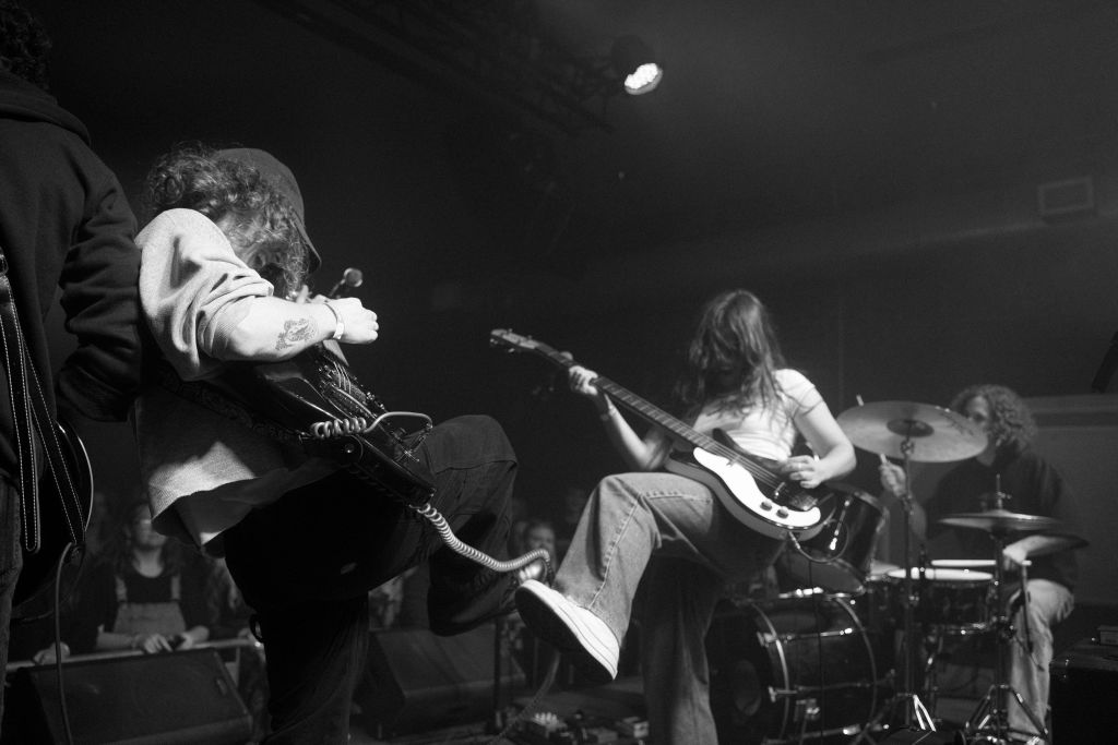 A dynamic black and white photograph captures a band in mid-performance, with musicians energetically playing guitars and drums on stage in Atlanta, Georgia.