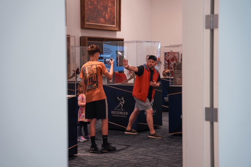 A young boy in an orange shirt takes a photo of a display case in a museum, while an adult in a red vest gestures towards another exhibit in Atlanta, Georgia.
