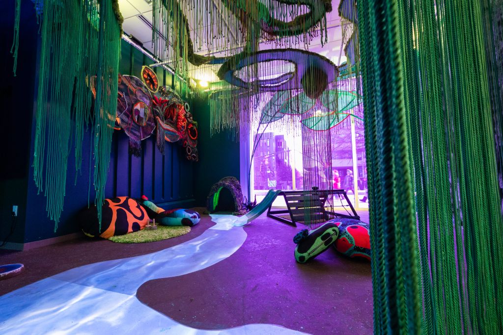 A vibrant, whimsical indoor play area with colorful inflatables, a slide, and a unique green, leafy ceiling installation in Atlanta, Georgia.