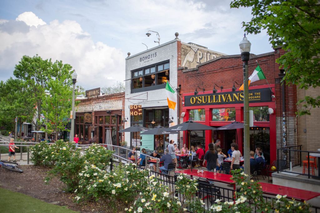 A vibrant outdoor dining area with colorful umbrellas and flags, surrounded by lush greenery and historic buildings in a charming town square in Atlanta, Georgia.