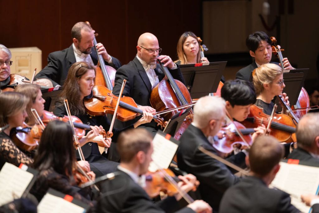 A diverse orchestra dressed in formal attire performs a classical piece with precision and passion in Atlanta, Georgia.