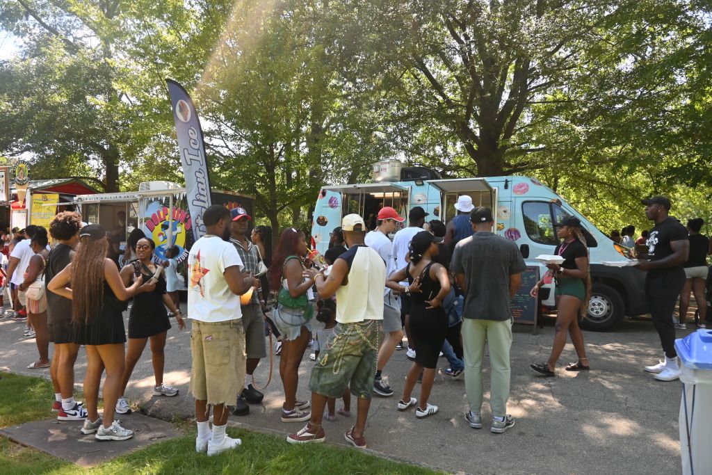 A lively outdoor food truck festival with a diverse crowd enjoying sunny weather under the shade of trees in Atlanta, Georgia.