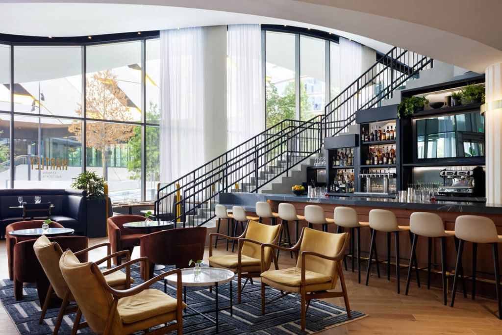 A modern, spacious bar and lounge area with large windows, a curved staircase, and a variety of seating options in Atlanta, Georgia.
