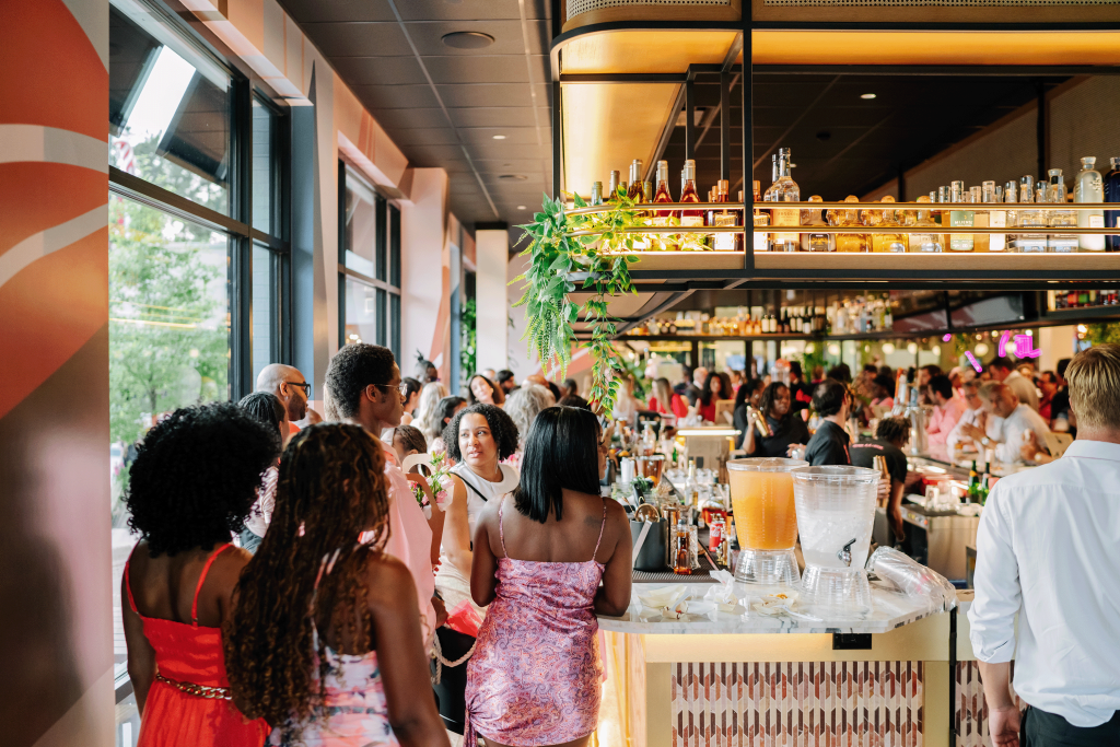 A lively crowd enjoys cocktails and conversation at a trendy rooftop bar with vibrant decor and expansive city views in Atlanta, Georgia.