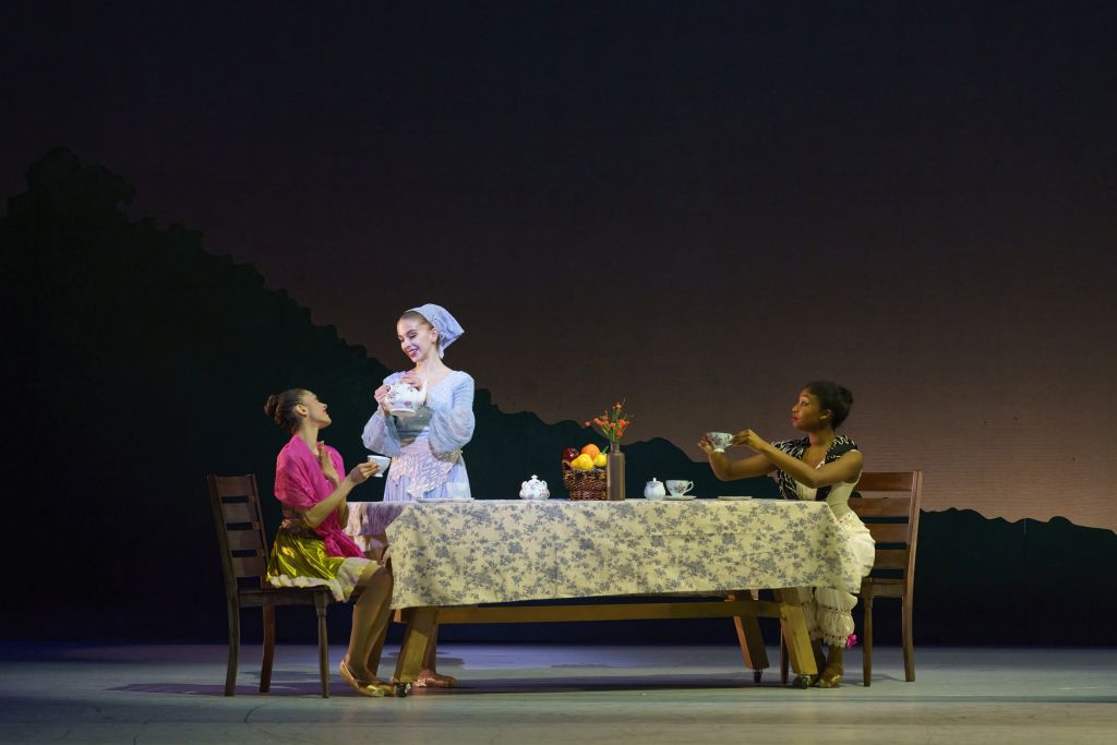 Three women dressed in period costumes sit at a table set for tea, with one serving tea to the others in Atlanta, Georgia.