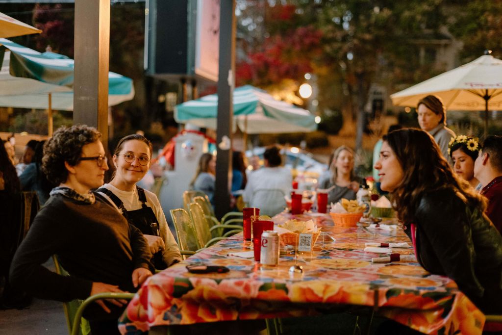 A group of women enjoy a casual outdoor dinner under colorful umbrellas at a restaurant in Atlanta, Georgia.