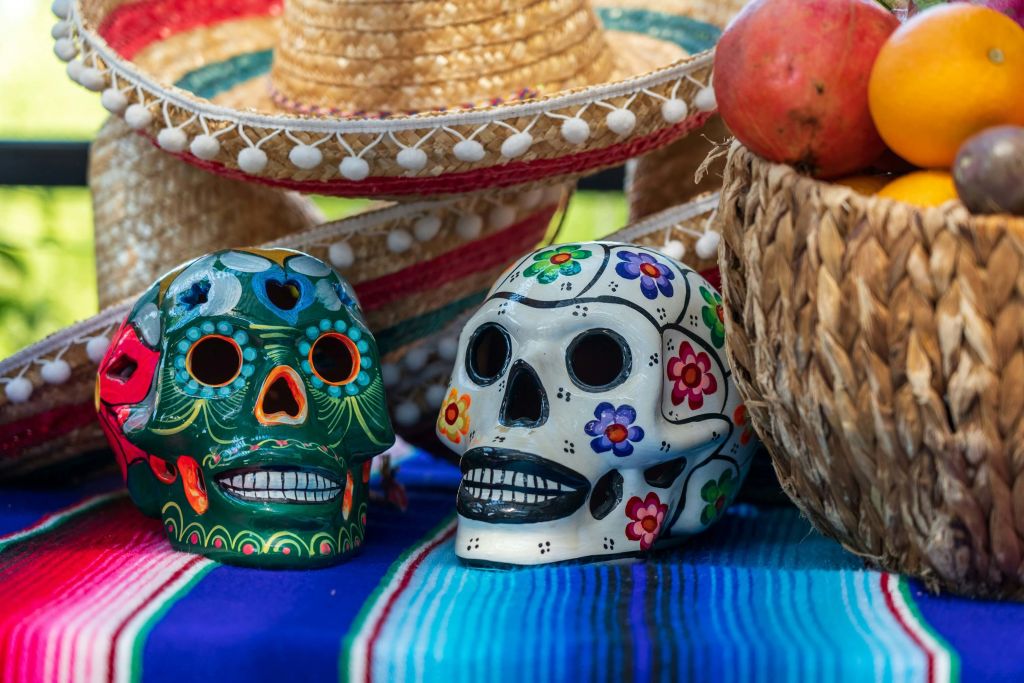 Colorful sugar skulls and fruit-filled basket displayed on a vibrant Mexican blanket with sombreros in the background in Atlanta, Georgia.