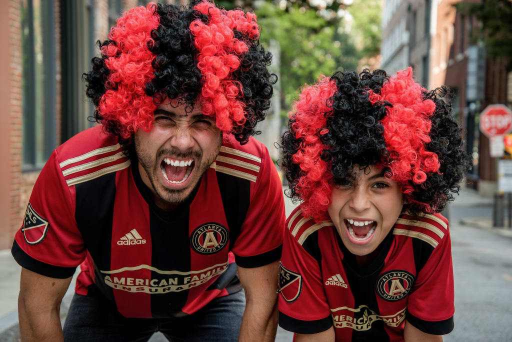 Two people wearing Atlanta United soccer jerseys and red-black wigs cheer enthusiastically in Atlanta, Georgia.