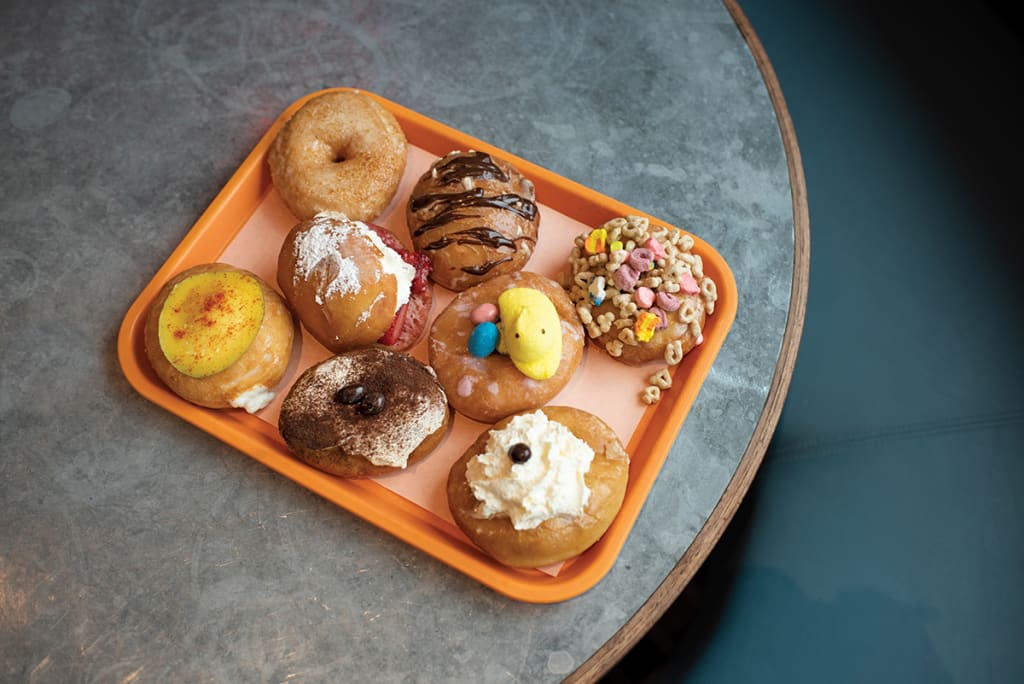 An assortment of eight colorful and uniquely decorated doughnuts on an orange tray in Atlanta, Georgia.
