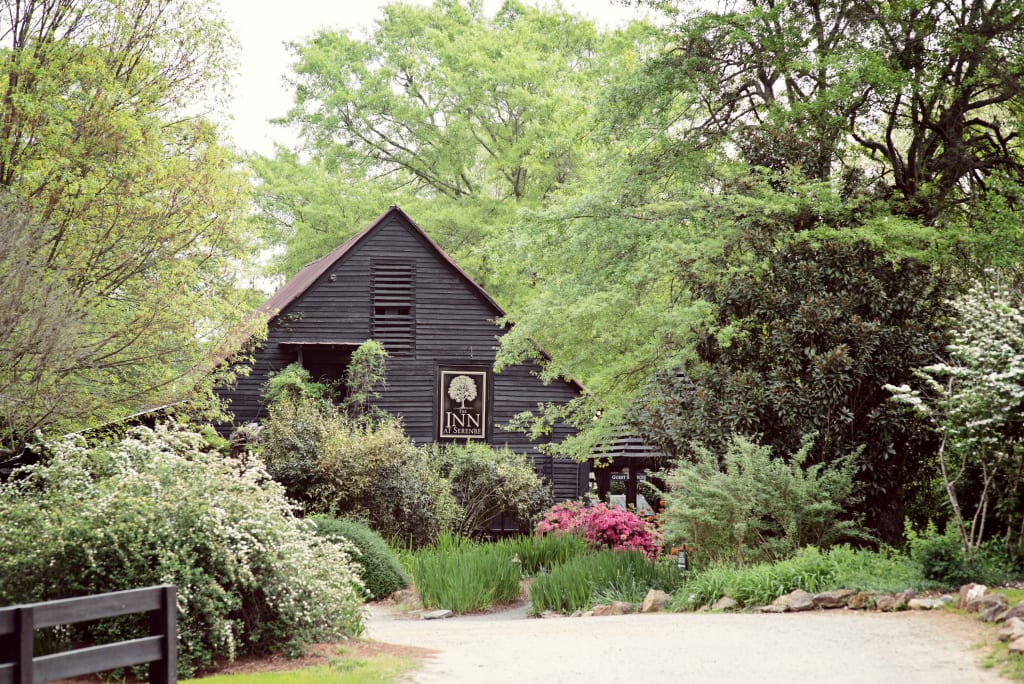 A quaint, dark wooden house nestled among lush greenery and blooming flowers in Atlanta, Georgia.