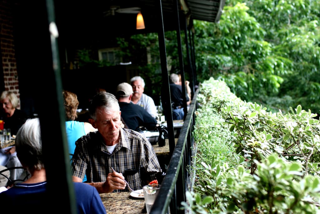 Elderly man in plaid shirt eating at outdoor restaurant with lush greenery in Atlanta, Georgia.