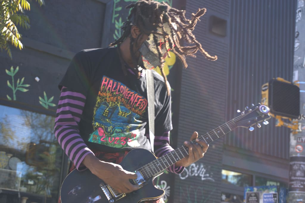 10 Reasons to Celebrate Halloween at Little 5 Points in Atlanta 2 A musician with dreadlocks and a mask plays an electric guitar on a city street in Atlanta, Georgia.