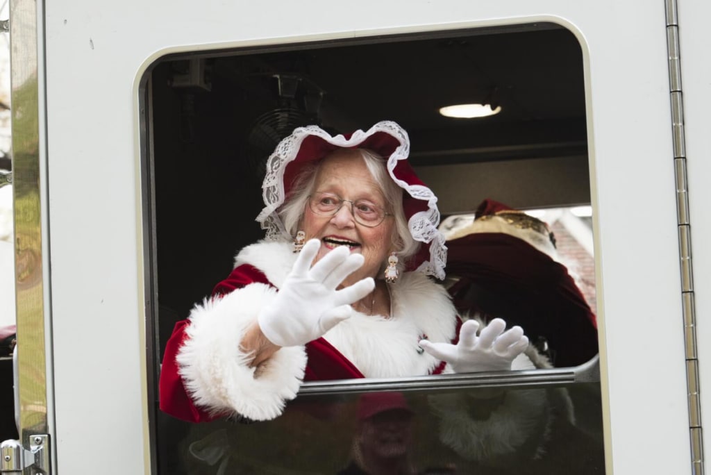 Elderly woman dressed as Mrs. Claus waves cheerfully from a vehicle window in Atlanta, Georgia.