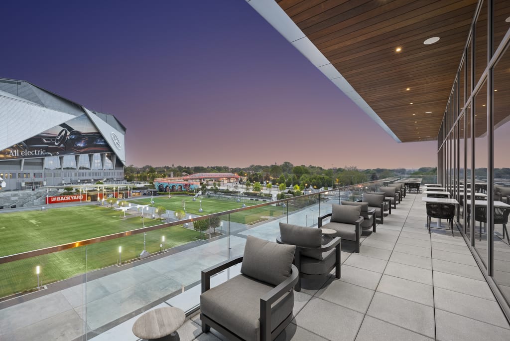 A rooftop terrace with modern furniture overlooks a vibrant stadium and cityscape at dusk in Atlanta, Georgia.
